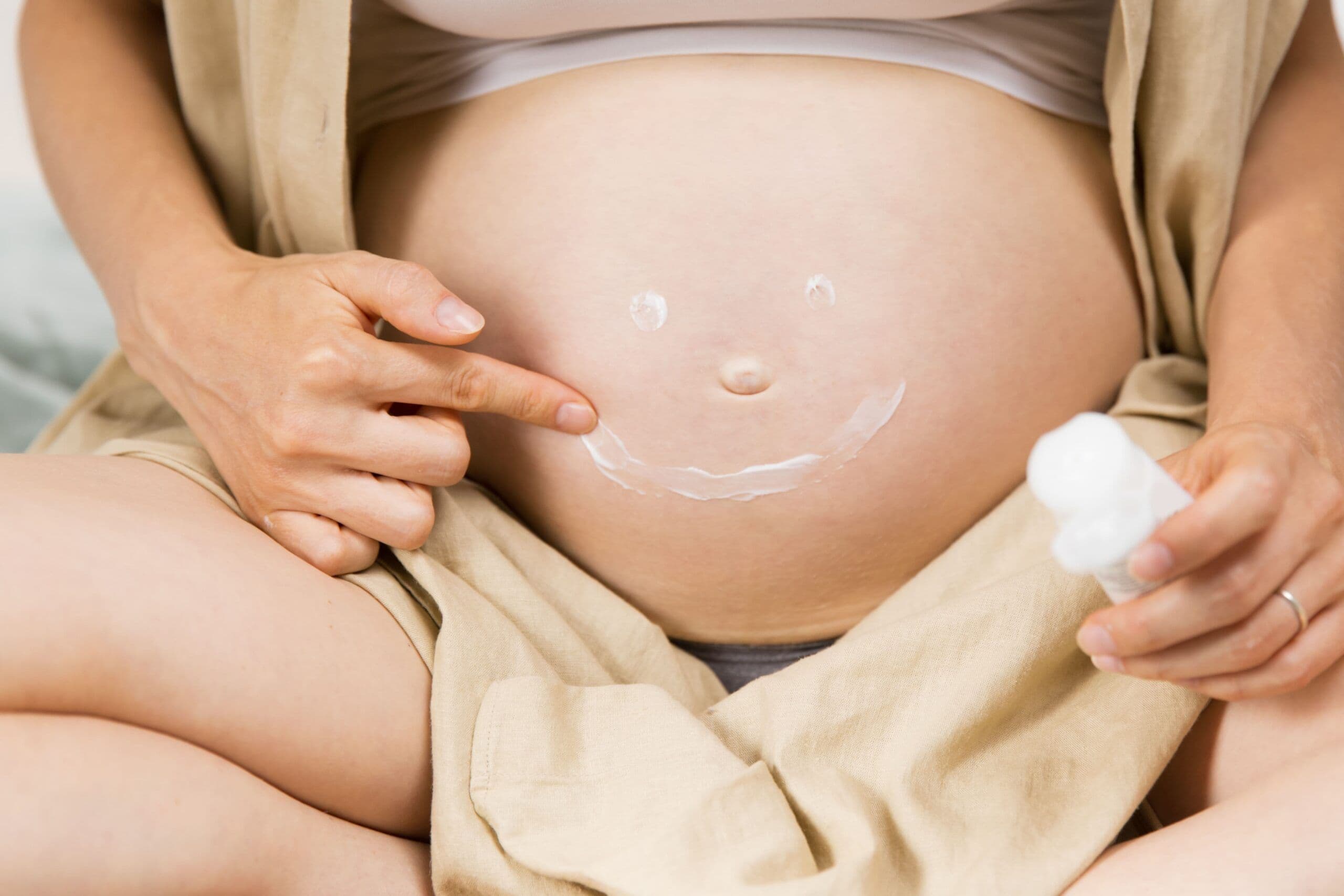 Fotografia de uma mulher grávida passando creme hidratante na barriga. O texto na imagem diz: Como cuidar da pele para reduzir o risco de estrias na gravidez: hidratação, ganho de peso e fatores genéticos